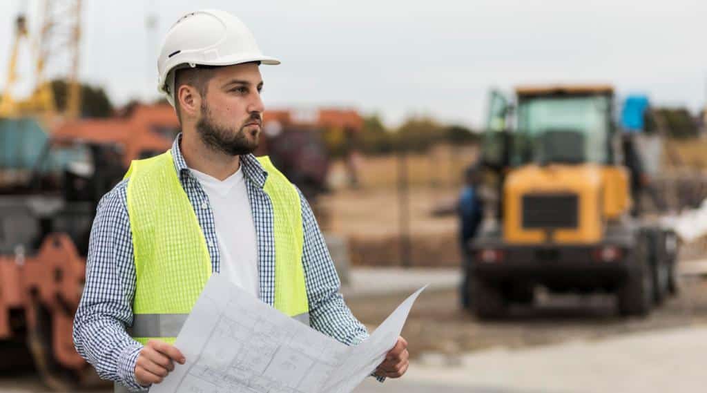 Engenheiro com capacete e planta de obra em canteiro de obras